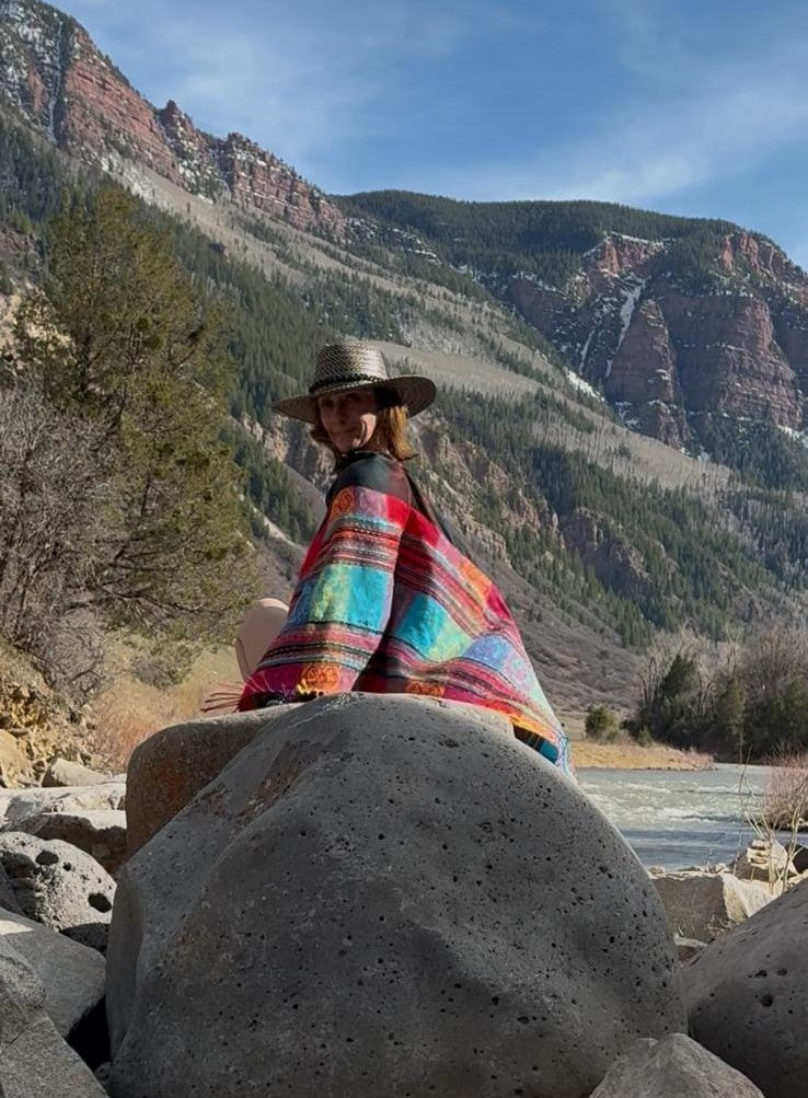 Harmonee on the rocks in the striped poncho scarf while travelling